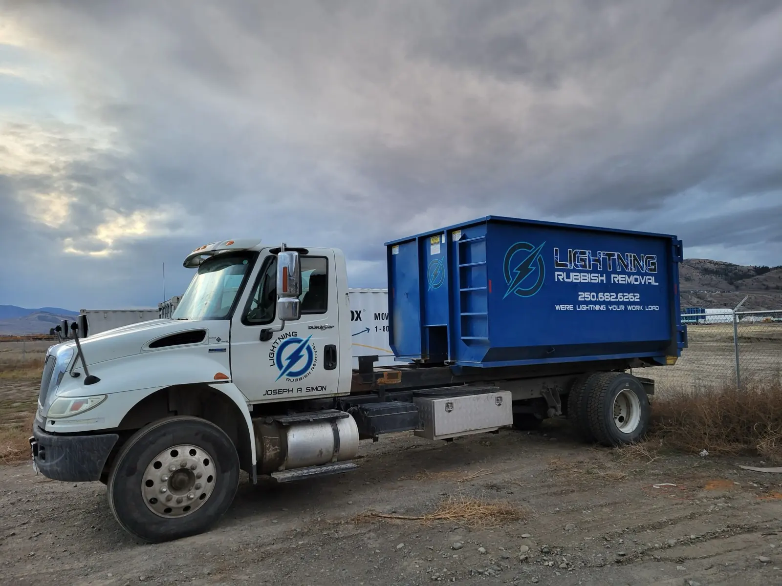 Lightning Rubbish Removal roll-off truck carrying a blue Lightning bin on the hills outside Kamloops